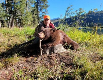 A male nonresident hunter poses next to a mountain lake with his color phase black bear.